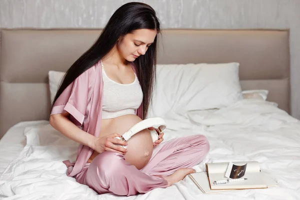 Mujer embarazada sosteniendo auriculares en su vientre — Foto de Stock