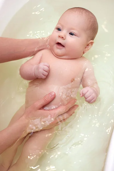 Mother bathes her baby in a white small plastic tub Stock Photo