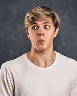 Gri arka planda kafası karışmış genç beyaz bir adam..