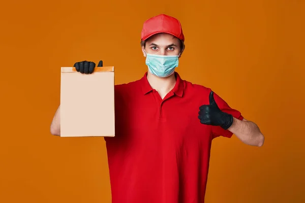 Leverancier met rood masker, lege kartonnen doos — Stockfoto