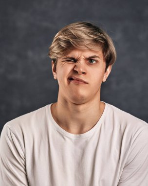 Koyu gri arka planda suratını buruşturan yakışıklı adam.