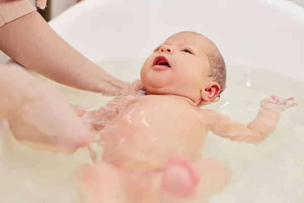 母亲在一个白色的小塑料桶里给婴儿洗澡 — 图库照片