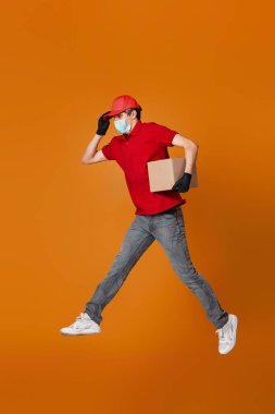 Yüzü maskeli bir teslimatçı elinde karton kutuyla atlıyor.