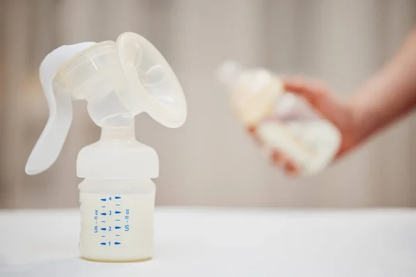 Manual breast pump on background of hand with bottle with milk — Stockfoto