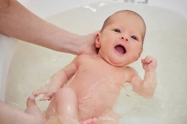 Мать купает своего ребенка в белой маленькой пластиковой ванне — стоковое фото