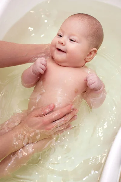 Мать купает своего ребенка в белой маленькой пластиковой ванне — стоковое фото