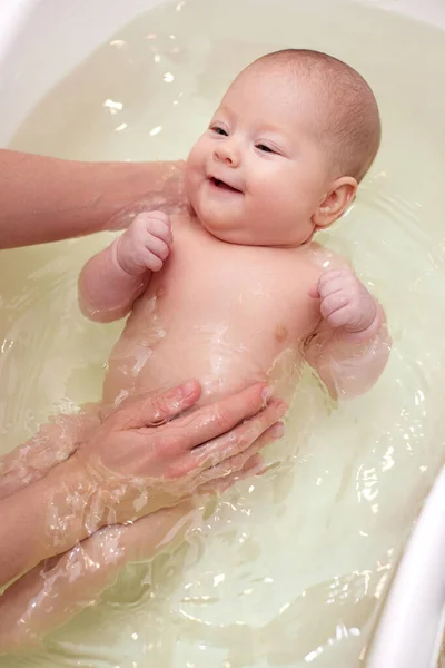 Mother bathes her baby in a white small plastic tub Royalty Free Stock Images