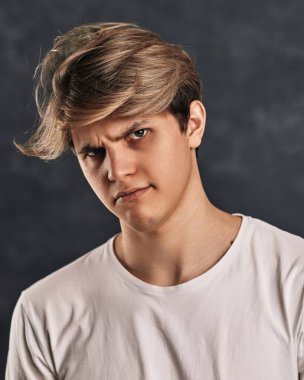 Gri arka planda üzgün, ciddi bir genç adam. İnsan duyguları, yüz ifadeleri.