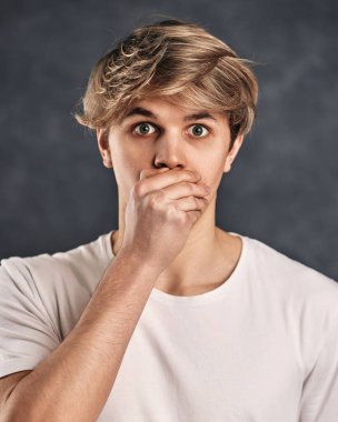 Gri arka planda beyaz tişörtlü, şık saç kesimi olan, korkmuş genç bir adam..