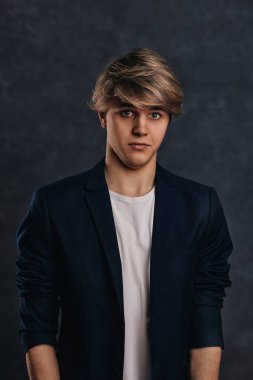 Gri arka planda ceketli, modern saç kesimi olan genç ve yakışıklı bir adam..