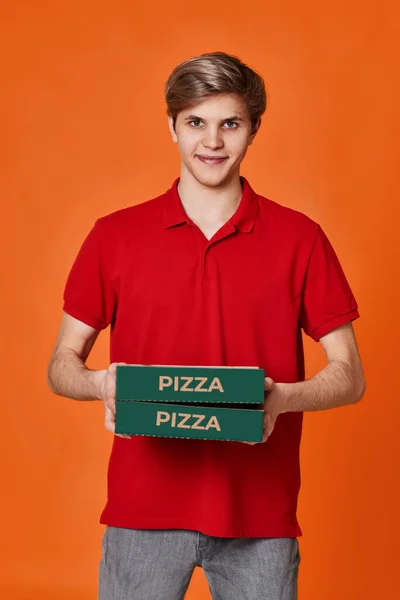 赤いTシャツのピザ配達人オレンジの背景に隔離された段ボール箱を保持 — ストック写真