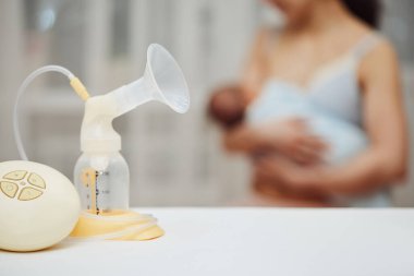 Anne kucağında çocuğunun arka planında anne sütü olan göğüs pompası. Annelik ve çocuk bakımı.