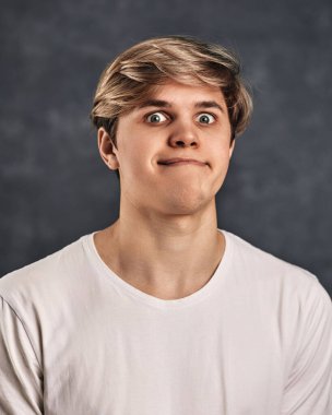 Koyu gri arka planda suratını buruşturan genç yakışıklı adam.