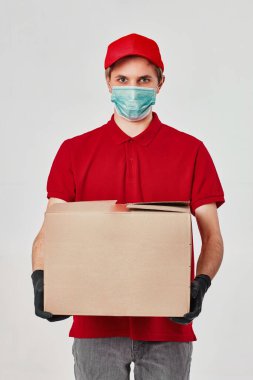 Kırmızı şapkalı teslimatçı, boş tişört, maske, beyaz arka planda karton kutu tutan eldivenler.