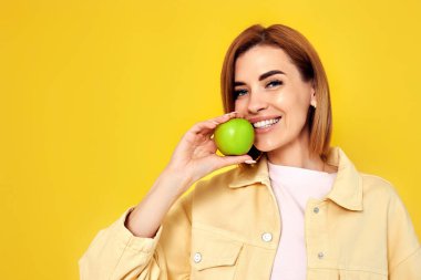 Sarı arka planda yeşil elma tutan gülümseyen sarışın kadının portresi. kopyalama alanı. Sağlıklı yemek.