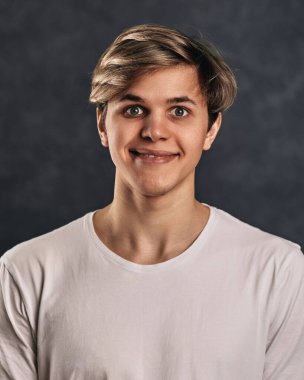 Beyaz tişörtlü, gri arka planda gülümseyen genç yakışıklı adam. İnsan duyguları, yüz ifadeleri.