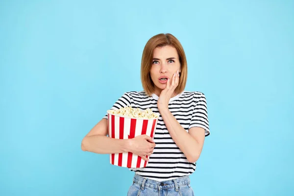 feared frightened woman watching movie film, holding bucket of popcorn isolated on blue background
