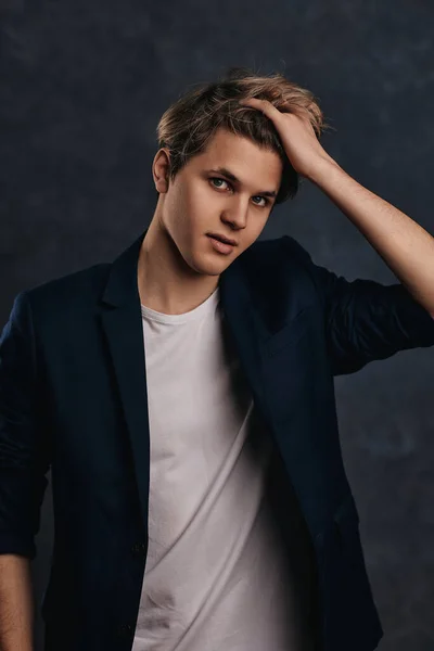 young handsome man with modern haircut in a jacket looking at the camera on gray background.