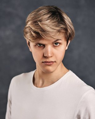 Modern saç kesimli genç yakışıklı gri arka planda kameraya bakıyor..