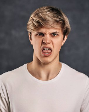 Gri arka planda olumsuzluğu ifade eden genç bir adamın portresi. Bu iğrenç.