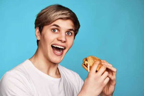 Joven Muy Hambriento Sosteniendo Sabrosa Hamburguesa Aislada Sobre Fondo Azul — Foto de Stock