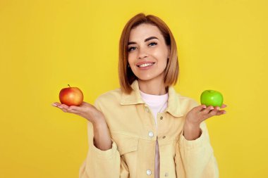 Sarı arka planda yeşil ve kırmızı elmalar tutan gülümseyen sarışın kadın..
