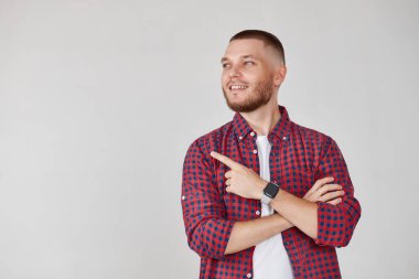 Gülümseyen yakışıklı sakallı adam gri arka planda izole edilmiş bir ürünü sunmak için kenarı işaret ediyor.