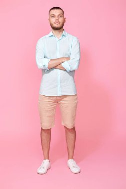 Mavi tişört giyen genç beyaz adam pembe arka planda izole bir şekilde el ele tutuşuyor. Tam uzunluk