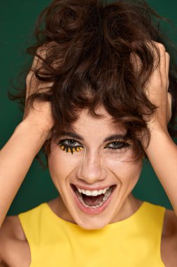 Sarı elbiseli mutlu kıvırcık kadın portresi. Yeşil arka planda ağzı açık.