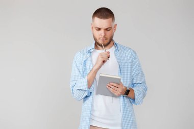 ciddi mavi tişörtlü yakışıklı bir adam elinde defter tutuyor, plan yapıyor ya da soru soruyor.