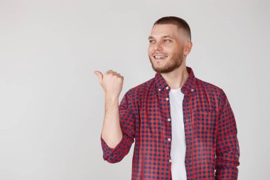 Genç yakışıklı sakallı adam, gri arka planda izole edilmiş bir ürünü sunmak için kenarı işaret ediyor.