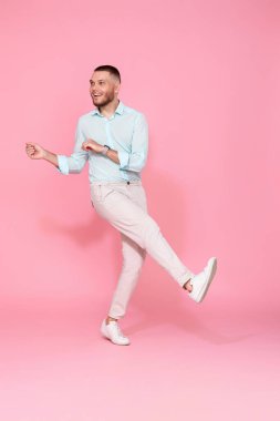 Pastel pembe arka planda yalnız dans eden mavi tişörtlü yakışıklı adam. Tam uzunluk
