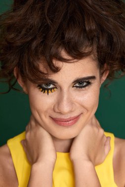 Yeşil arka planda sarı elbiseli yaratıcı kıvırcık kadın..