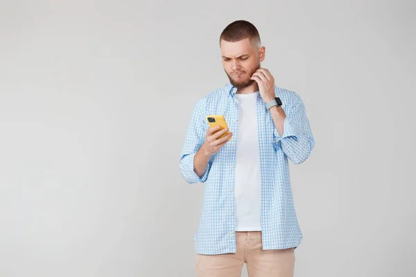 Pensive young man looking at mobile cell phone surfing internet. copy space