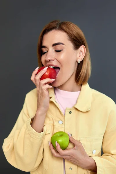 Smiling Blonde Woman Holding Green Red Apples Yellow Background — Stockfoto