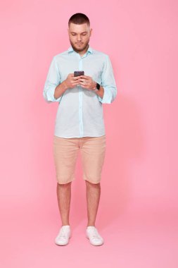 Yazın mavi tişörtlü mutlu ve sakallı bir adam cep telefonuyla mesajlaşıyor.