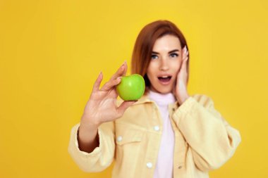 surprised cheerful woman holding green apple isolated on yellow background. focus on apple