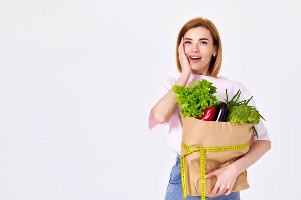Surprised Slim Woman Holds Paper Bag Vegetables Measuring Tape White — Foto de Stock