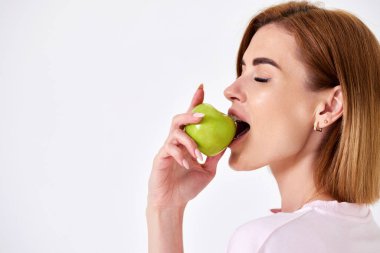 Portrait of a cheerful woman eating green apple isolated on white background. copy space