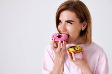 Gülümseyen güzel sarışın kadın beyaz arka planda izole edilmiş donutları ısırıyor. Boşluğu kopyala