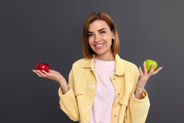 Sarı arka planda yeşil ve kırmızı elmalar tutan gülümseyen sarışın kadın..