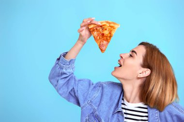 so delicious. young woman eating pizza slice and looking delighted on blue background. copy space