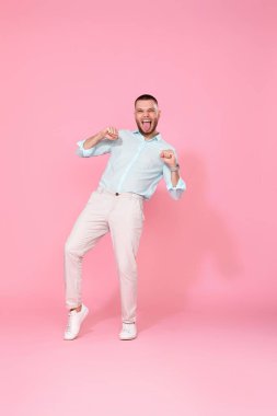 Pastel pembe arka planda yalnız dans eden mavi tişörtlü yakışıklı adam. Tam uzunluk