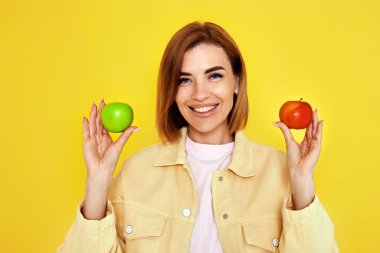 Sarı arka planda yeşil ve kırmızı elmalar tutan gülümseyen sarışın kadın..