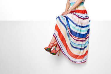 female legs wearing long striped summer dress and pink high heels shoes sitting on white banner. copy space.