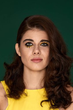 Yeşil arka planda sarı elbiseli yaratıcı kıvırcık kadın..