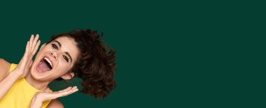 portrait of surprised amazed shocked young woman in yellow dress starring with opened mouth on green background. copy space