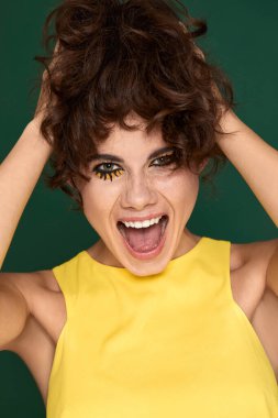 portrait of happy exited pretty young womanwith fun make-up in yellow dress starring with opened mouth on green background