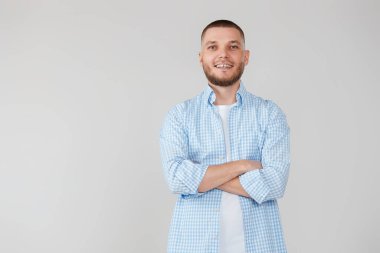 Gülümseyen genç adam gri stüdyo arka planında çapraz kollarla poz veriyor.