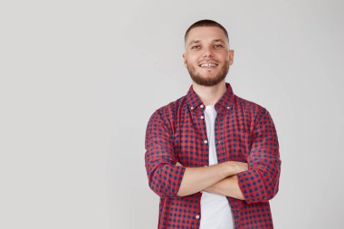 Gülümseyen genç adam gri stüdyo arka planında çapraz kollarla poz veriyor.
